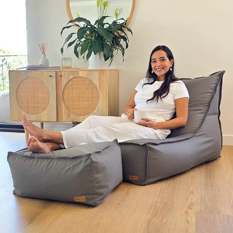 Mooi Living Single Boss Bean Bag in Mocha shown with coordinating cotton canvas ottoman in a modern living room. Model is seated in the bean bag with feet up on the ottoman, holding a cup of coffee.