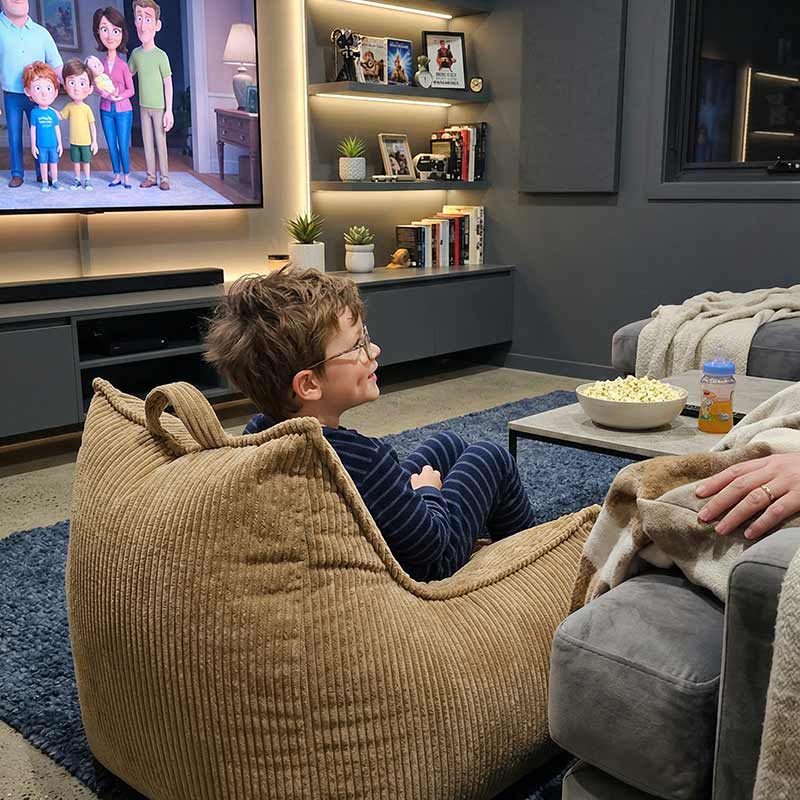 Lifestyle image of the Mini Cord Bean Bag Chair in Caramel with a little boy in a theatre room.