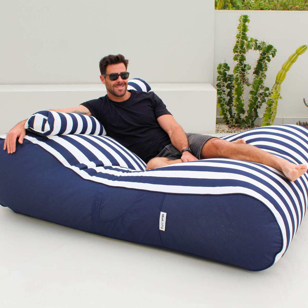 Man reclining on a Mooi Living Navy Stripe Nevaeh double outdoor bean bag sunbed with a matching bolster cushion, MOSTNEVBB-STRI-NAV