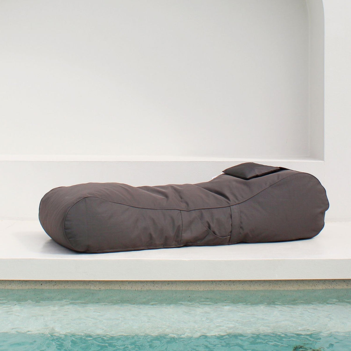 Side view of a Mooi Living Oyster Black Isla outdoor bean bag sunlounger with a matching pillow beside a pool, MOISLABB- OYSB