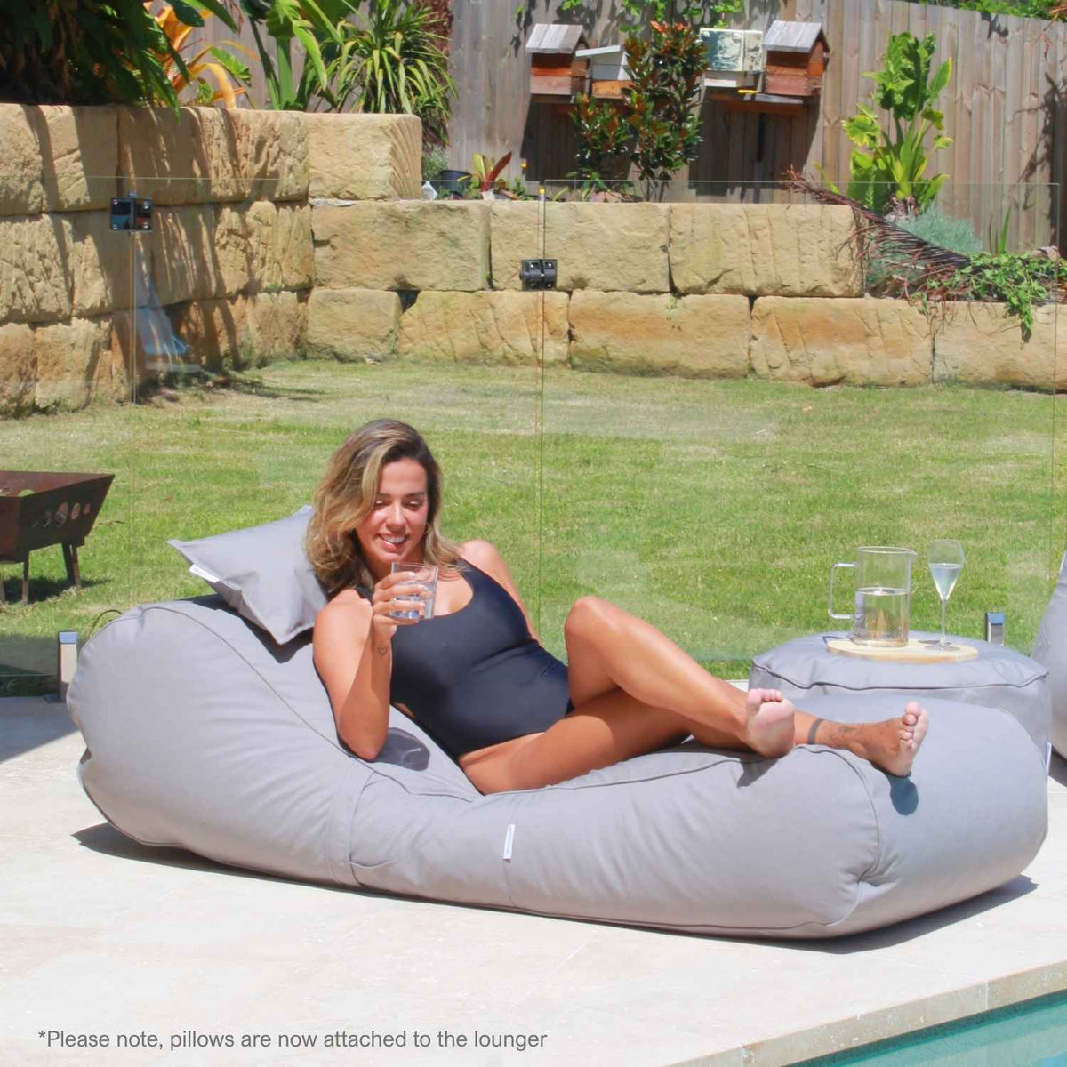 Woman holding a drink while relaxing on a Mooi Living Pumice Stone Isla outdoor bean bag sunlounger beside a matching ottoman, MOISLABB-PUMSTO