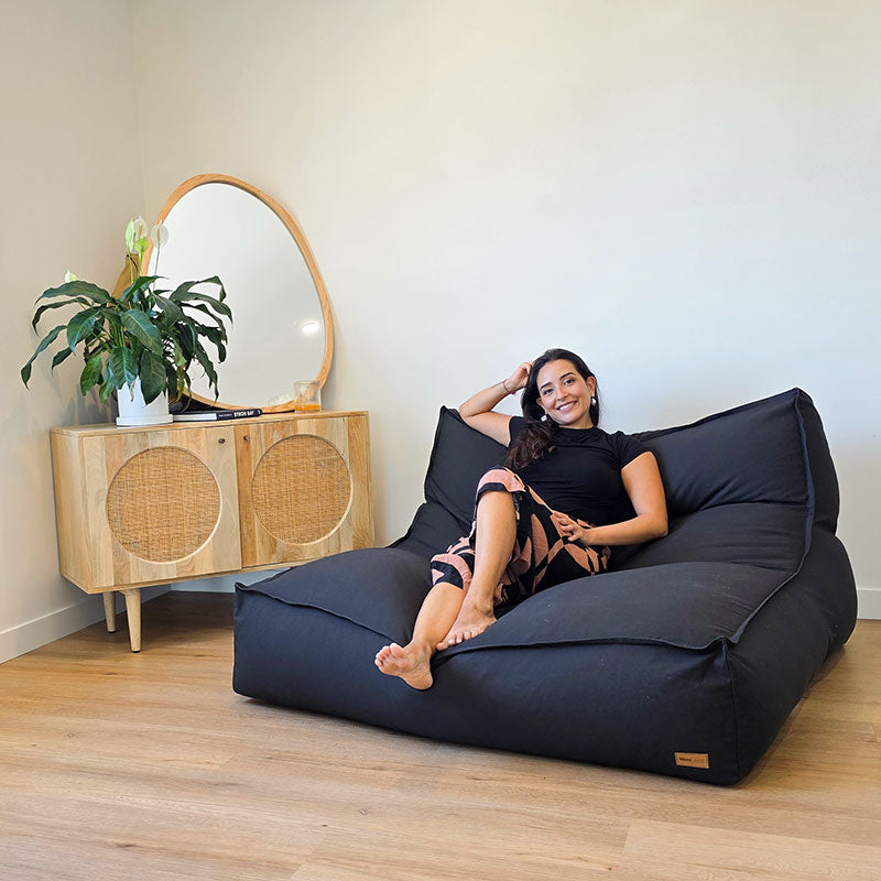 Black Double Boss structured indoor double seater by Mooi Living in a minimalist interior, lady seated on the bean bag smiling at the camera.
