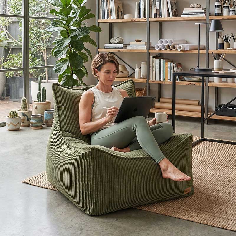Lifestyle image of Mooi Cord Bean Bag Chair in Olive Green with a woman using a tablet on the bean bag chair in a modern living room.