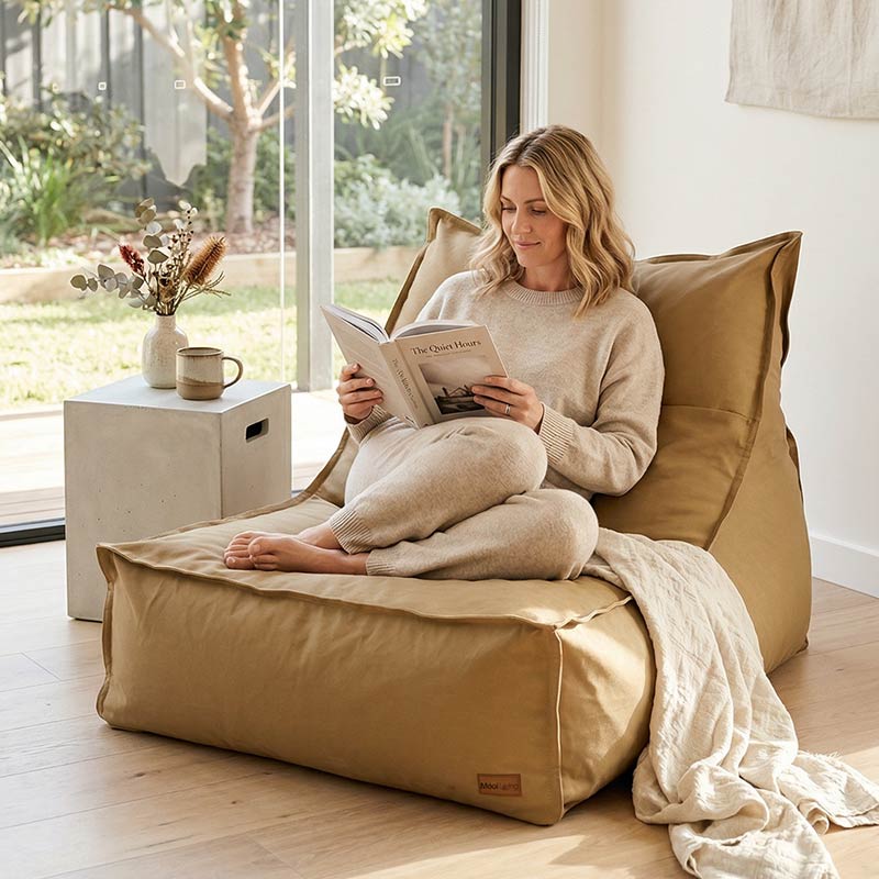 Lady sitting comfortably on a tan single boss bean bag chair, reading a book.