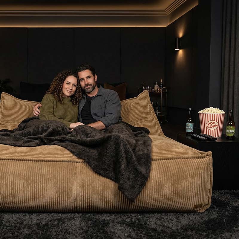 Lifestyle image of the Mooi Double Cord indoor bean bag by Mooi Living in Caramel with a couple sitting on it while relaxing in a theatre room.