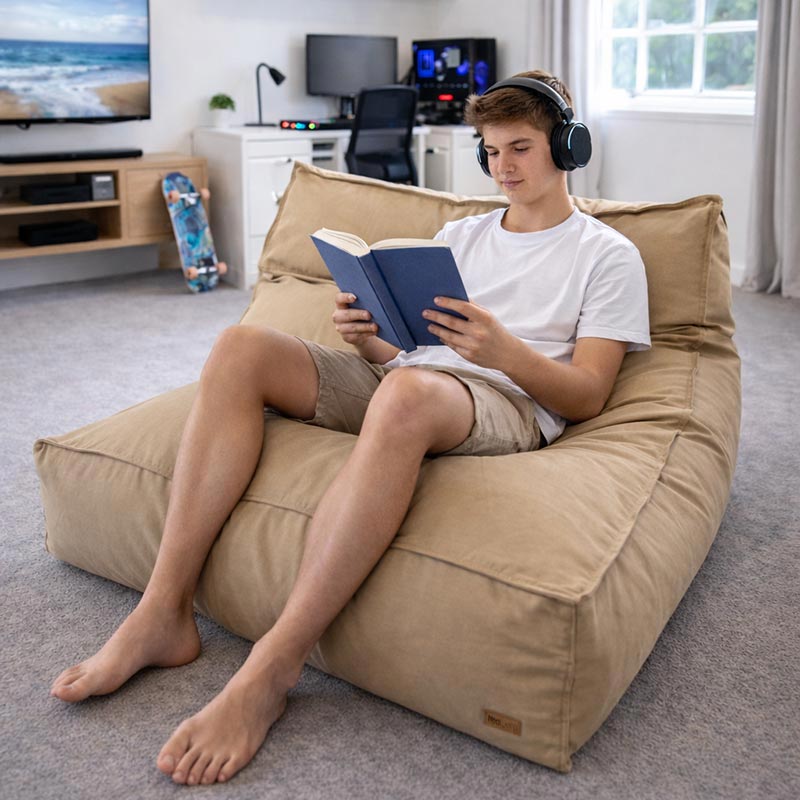 A teenager sitting comfortably in a Cotton Double Boss Bean Bag indoor bean bag by Mooi Living in Tan, reading.