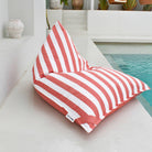 Mooi Living Blush reversible triangle outdoor bean bag beside a pool, showing its blush and white striped side, MOREVSTRIBB-BLUS