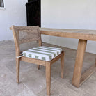A wooden dining chair with a striped cushion in sage green and white, positioned next to a matching wooden dining table on a stone tiled patio, MOO-STR-GRN-CHPAD