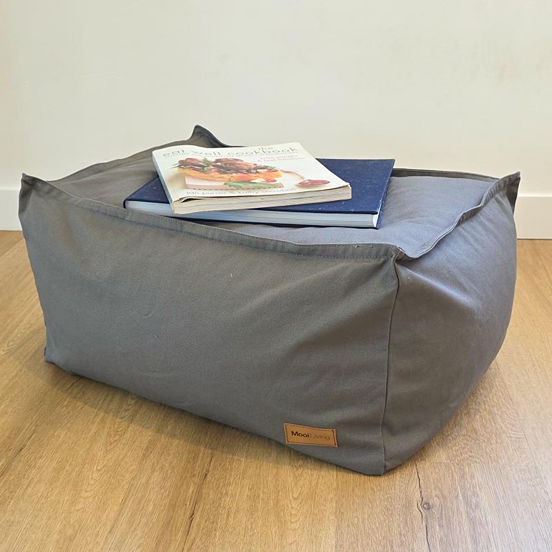 Mooi Living Mocha cotton canvas ottoman positioned in a contemporary living space with books resting on top.