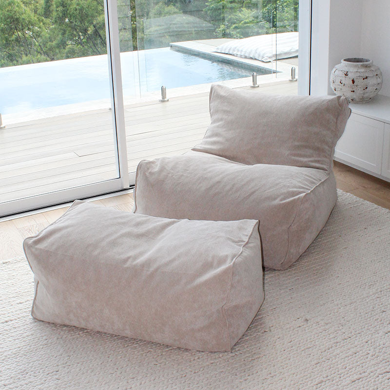 Brooklyn Corduroy bean bag chair in Natural Beige in a modern room with large windows and a pool view.