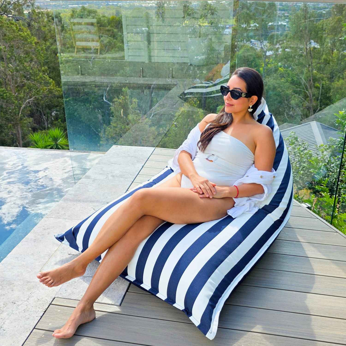 Woman reclining with legs extended on the navy and white striped side of a reversible triangle outdoor bean bag on a timber deck, MOREVSTRIBB-NAVY