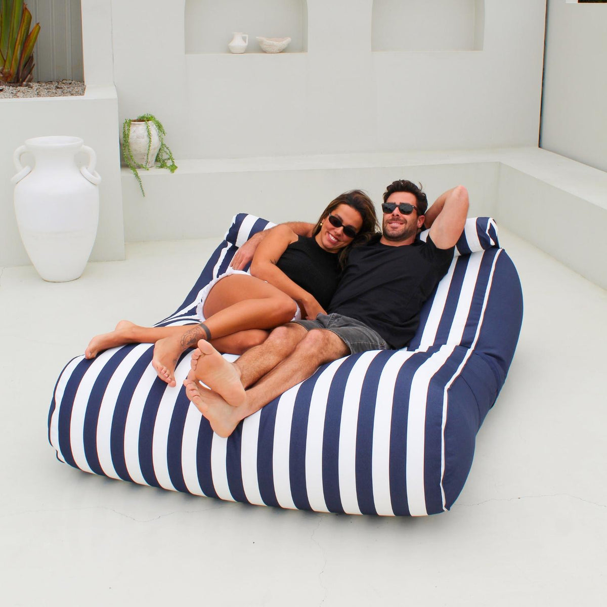 Couple relaxing together on a Navy Stripe Nevaeh double outdoor bean bag sunbed on a white patio, MOSTNEVBB-STRI-NAV