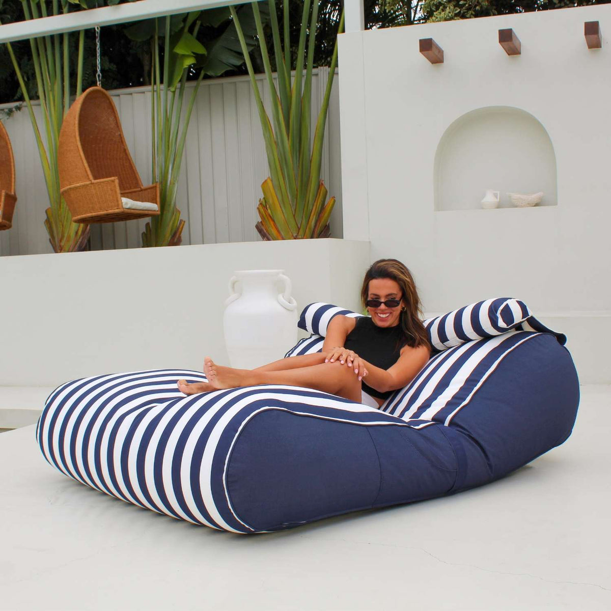 Woman lounging on a Mooi Living Navy Stripe Nevaeh double outdoor bean bag sunbed with navy side panels and white piping, MOSTNEVBB-STRI-NAV