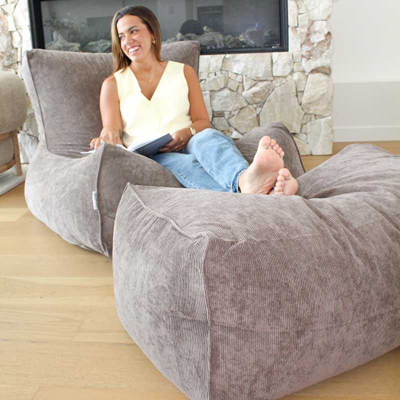 Brooklyn Corduroy bean bag chair and Ottoman in Nutmeg in a living room with a stone fireplace and television in the background.