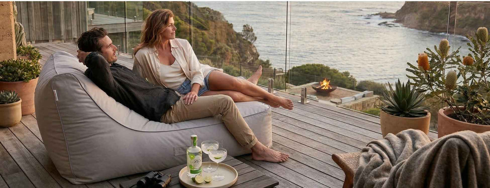 Two people sitting on an outdoor bean bag by Mooi Living, overlooking a scenic ocean view with a glass of wine.