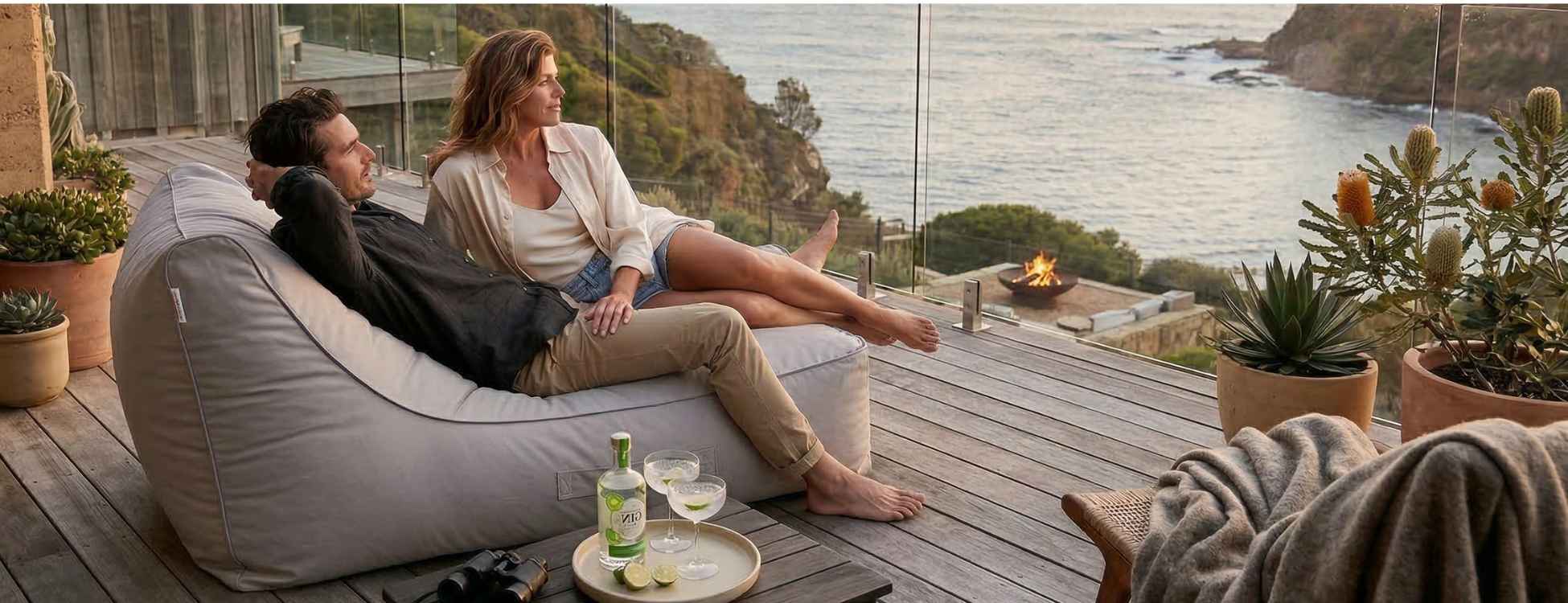 Two people sitting on an outdoor bean bag by Mooi Living, overlooking a scenic ocean view with a glass of wine.