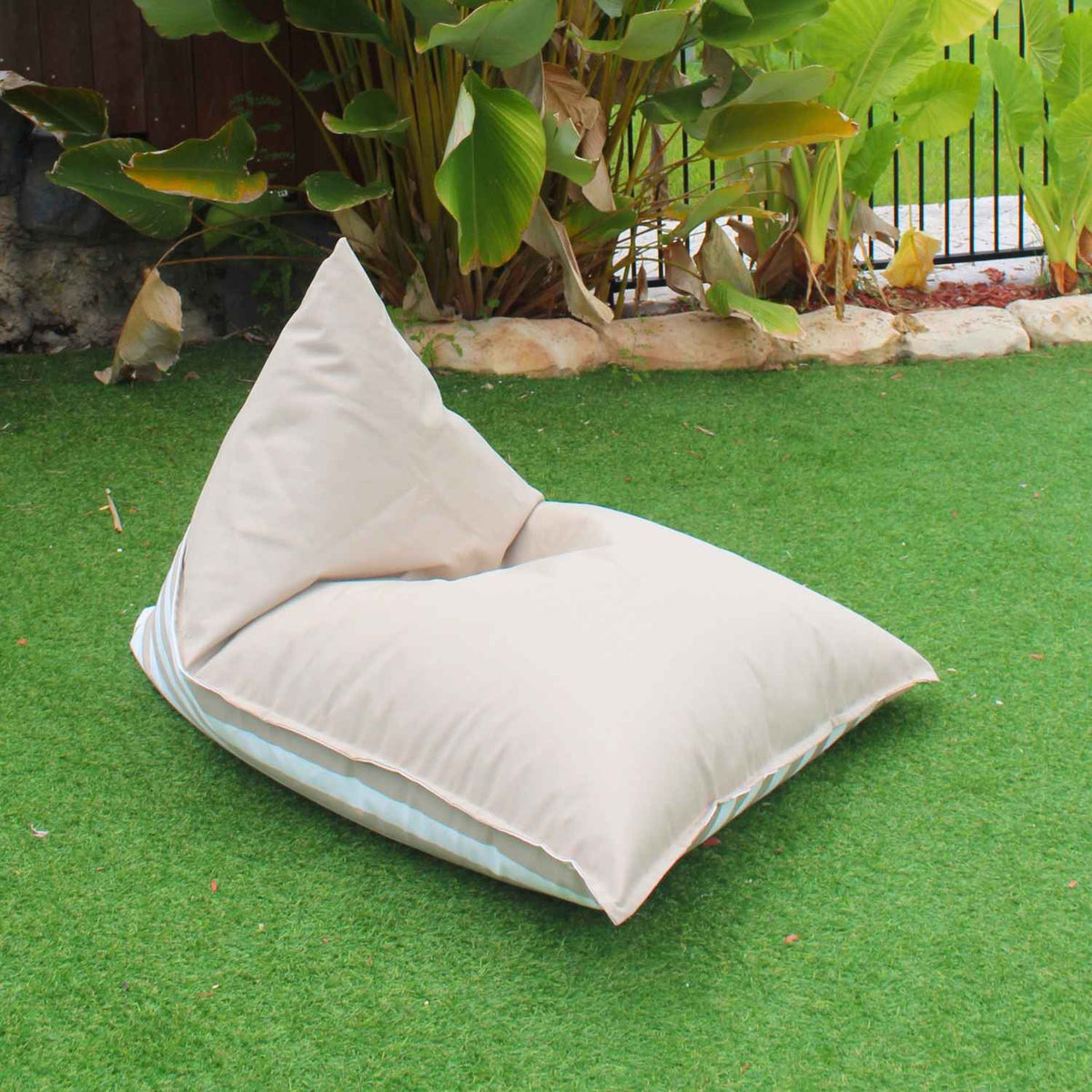 Mooi Living Taupe reversible triangle outdoor bean bag on grass, showing its plain taupe side with striped edging, MOREVSTRIBB-TPESTR