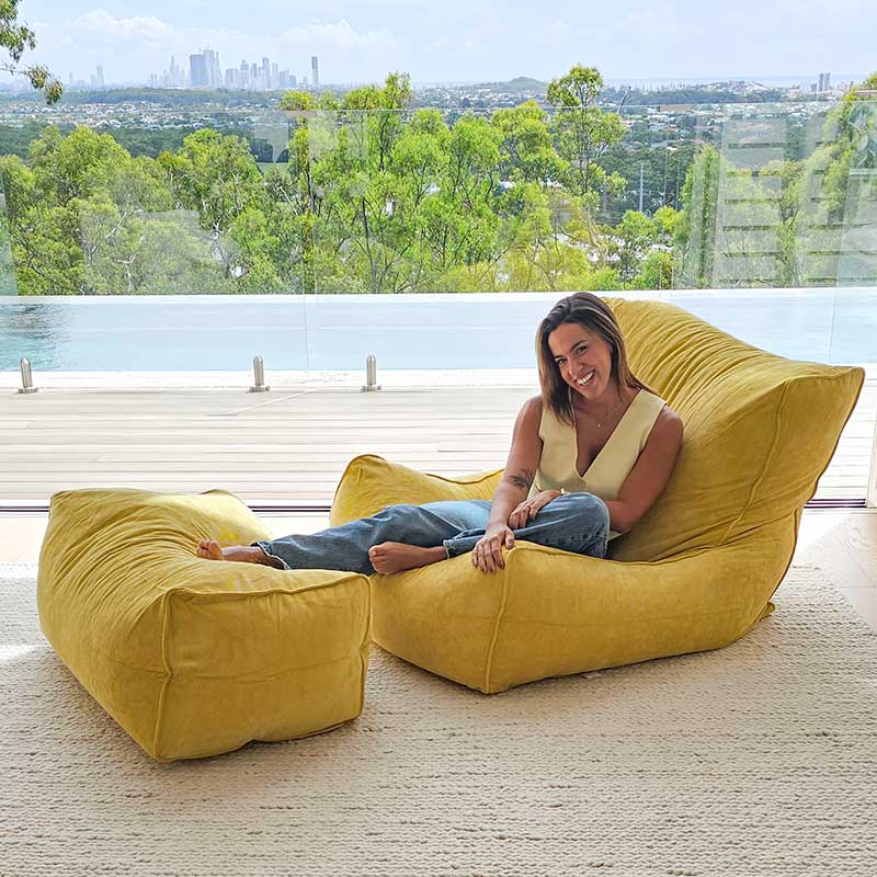 Brooklyn Corduroy bean bag chair in Yellow in a modern room with a woman sitting on the bean bag chair with a scenic view in the background