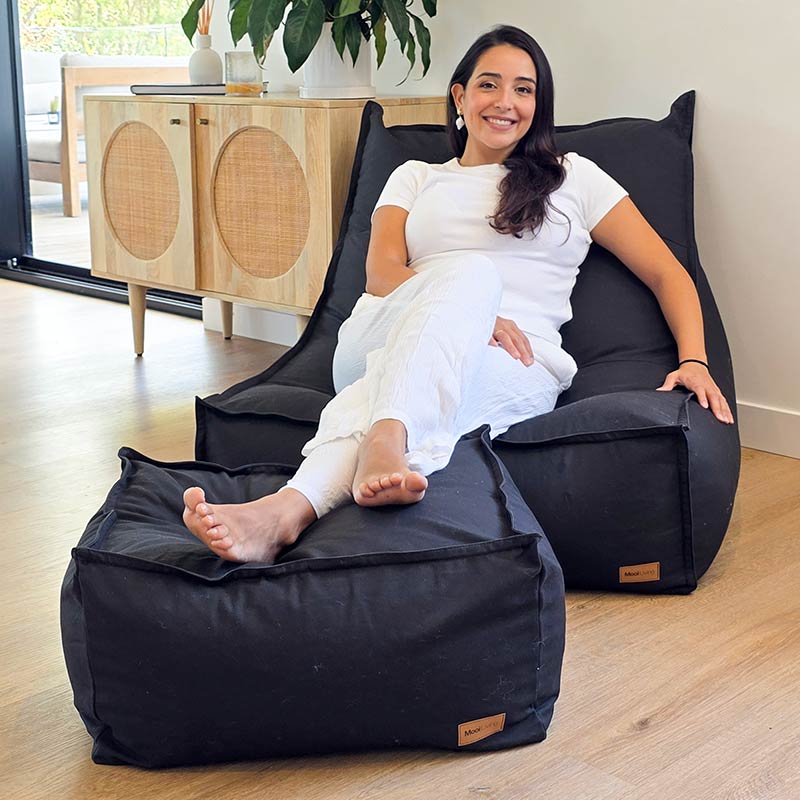 Model seated on a Mooi Living Black cotton canvas Single Boss paired with matching ottoman in a minimalist setting.