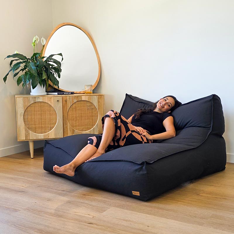 Woman seated on the Contemporary Black Double Boss Bean Bag by Mooi Living in a modern indoor setting.