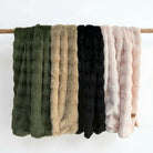 Set of five textured throws in green, beige, black, and pink on a wooden pole