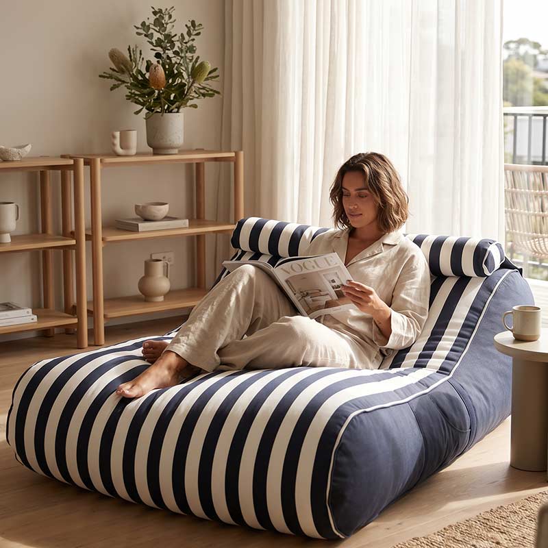 Woman reading a magazine on a Navy striped Nevaeh Sunbed outdoor bean bag by Mooi Living in a cozy living room.
