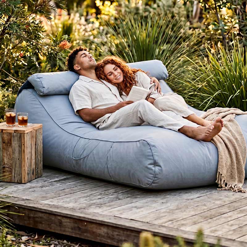 Couple relaxing on a Pumice Stone Nevaeh Sunbed outdoor bean bag by Mooi Living with drinks on a wooden table.