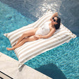 Taupe Stripe Santorini floating bean bag by Mooi Living positioned in a pool, model reclining on the outdoor bean bag float.