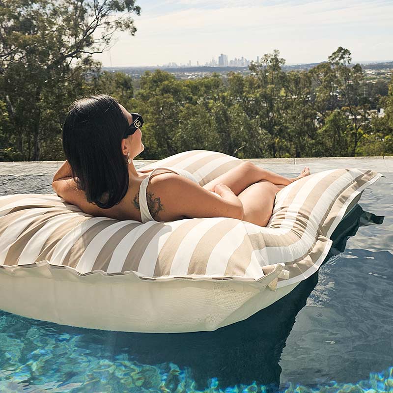 Taupe Stripe Santorini outdoor bean bag pool float by Mooi Living supporting model as she floats in a modern swimming pool.